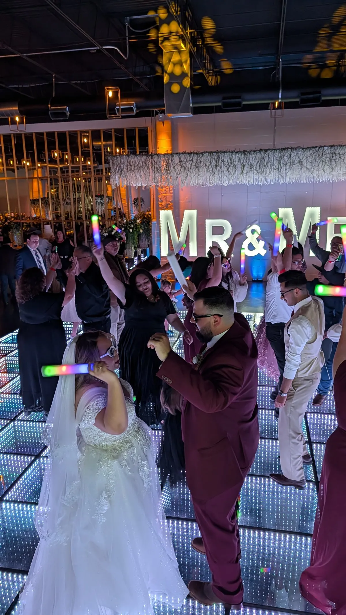 A bride and groom dancing with glow sticks on D'Venue's lit dance floor