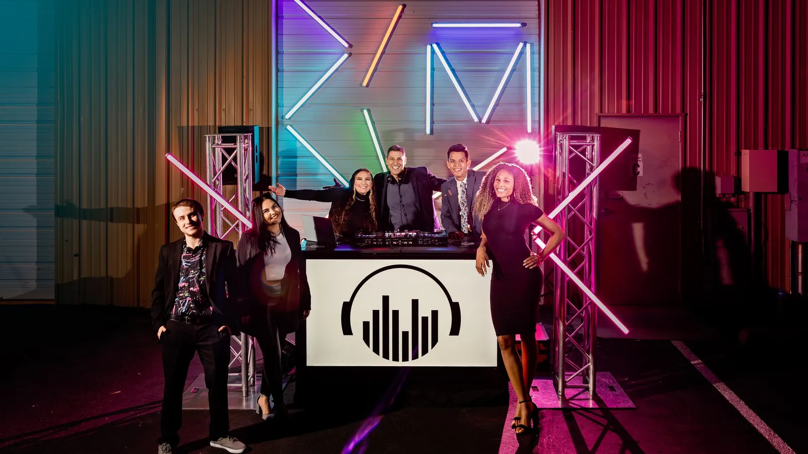 The Cutmaster Music team behind the DJ booth, lit by colorful neon
